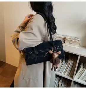 Detail of black rectangular shoulder bag with white stitching and plush bear charm