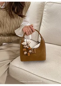 Detail der braunen Wildleder-Hobo-Tasche mit Plüschanhänger und Schleifen-Deko