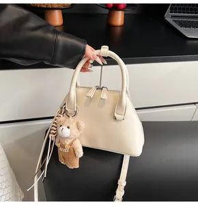 Detailed top view of beige shell shoulder bag with plush bear charm and leather tassels