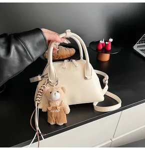 Detail view of cream shell crossbody bag with metal zipper and cute plush bear charm