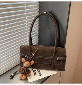 Close-up of vintage brown suede shoulder bag with white stitching and bear charm