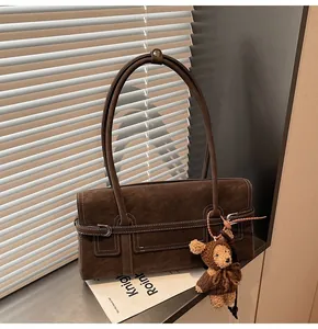 Close-up of retro brown suede shoulder bag with contrast stitching and plush bear charm