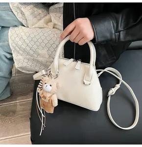 Detail of cream shell handbag with dual metal zippers and cute teddy bear pendant