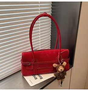 Detail of red suede shoulder bag with white contrast stitching and a cute bear pendant