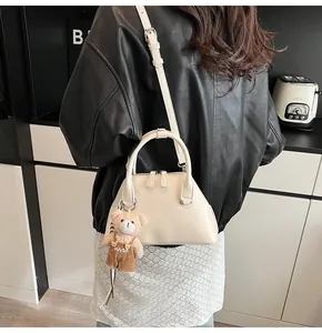Detail of cream shell handbag with cute plush bear charm and adjustable shoulder strap