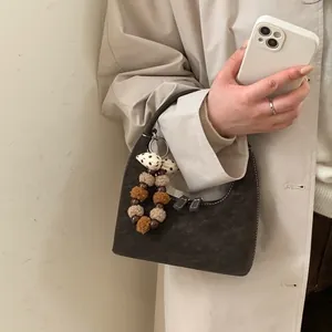Dunkelbraune Hobo-Tasche aus Wildleder mit weißen Nähten und flauschigem Anhänger