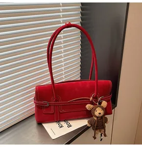 Close-up of red suede shoulder bag with contrast stitching and teddy bear charm accessory