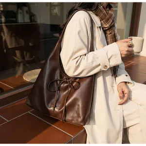 Detailed view of dark brown tote bag featuring a decorative drawstring bow and PU leather texture