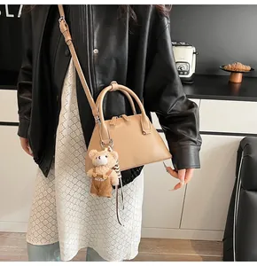 Detail of beige shell crossbody bag with a plush bear charm and round handle