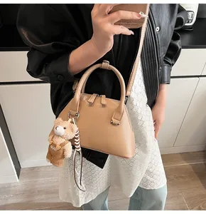 Detail of khaki shell crossbody bag with twin zippers and a cute plush bear charm
