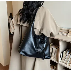 Detail of a large black matte leather tote bag with a drawstring bow on a shoulder strap