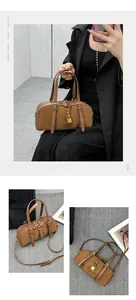 Detail view of brown Boston bag with matte leather texture, gold lock, and adjustable strap