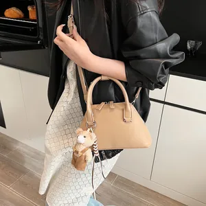 Chic beige shell-shaped crossbody bag with bear pendant shown on model in modern setting