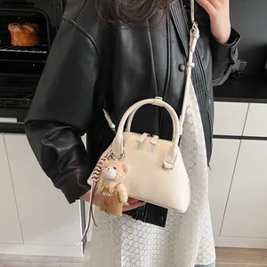 Chic beige shell-shaped crossbody bag with a cute bear charm and dual handles
