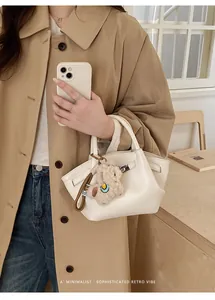 Detail der weißen Lychee-Ledertasche mit Plüsch-Anhänger und Metallschnallendesign