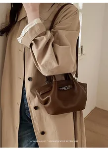 Dunkelbraune Tasche mit Litschi-Muster und silbernem Drehverschluss am Trenchcoat
