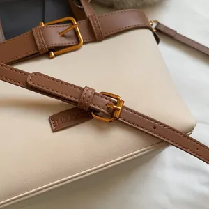 Dettaglio della borsa in pelle crema con tracolla marrone e fibbia dorata regolabile