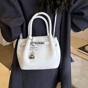 Weiße Bucket-Bag aus Lychee-Leder mit silbernem Schloss und Anhänger am Modell