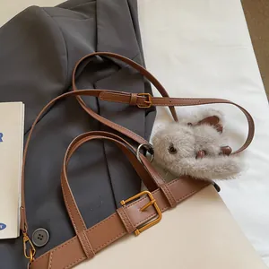 Dettaglio di un ciondolo di peluche su un cinturino in pelle marrone con fibbia dorata