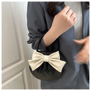 Dettaglio della borsa a mano tonda nera con fiocco in pelle color crema su modella