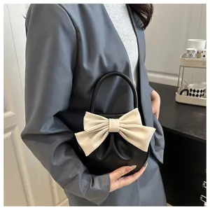Dettaglio di borsa a mano tonda nera con grande fiocco color crema e design a pieghe