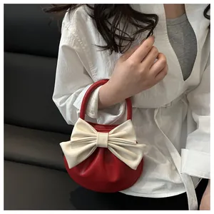 Dettaglio borsa a mano semicircolare rossa con grande fiocco color crema in pelle lucida