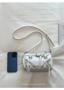 Close-up of white leather mini crossbody bag with silver buckles and studs next to a phone