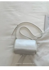 Close-up of a minimalist cream shoulder bag with strap buckle detail on white fabric