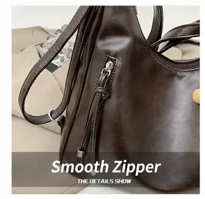 Detail of smooth metal zipper and long leather pull on the dark brown tote bag