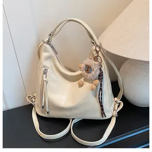Detail view of cream white hobo bag with fringe zipper and brown plush bear charm