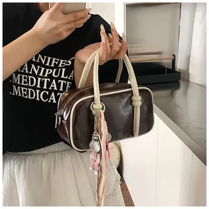 Détail du sac Boston marron foncé avec bordure crème, double fermeture et pendentif déco
