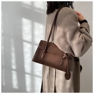 Brown leather underarm bag styled with a beige coat in a natural light setting