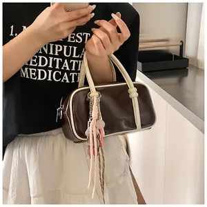 Détail du sac Boston marron avec poignées crème et breloque décorative en corde rose