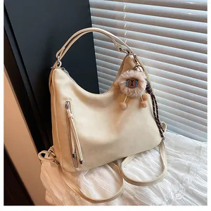 Detail of cream multi-way bag featuring a plush sheep pendant and decorative long zippers