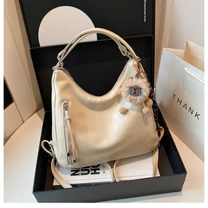 Detail of cream matte faux leather hobo bag with side zipper and plush charm in a gift box