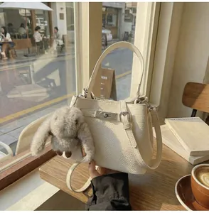 Detail of cream lychee leather bucket bag with silver buckle and plush rabbit charm