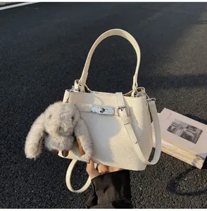 Detail of white lychee leather bucket bag featuring a silver lock and cute bunny pendant