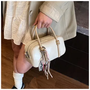 Détail du sac Boston crème avec longues poignées et breloque logo élégante avec corde tressée