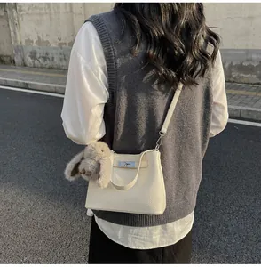 Detail of cream leather bucket bag with silver clasp and plush bunny charm on shoulder