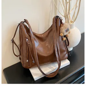 Detail of dark brown vintage tote with fringe zipper and plush bear charm on white background