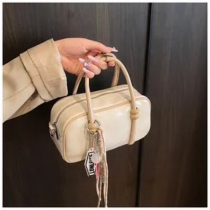 Détail du sac Boston crème avec texture en cuir PU, étiquette logo et pompon élégant