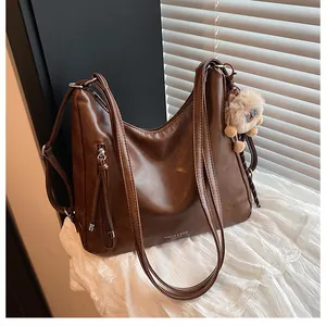 Detail of dark brown leather tote featuring zipper pocket with long tassel and lion plush charm