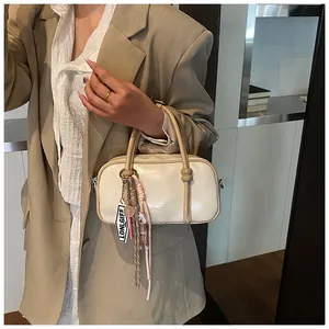 Détail du sac Boston crème avec finition polie et pendentif logo élégant et chic