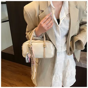 Détail d'un sac Boston blanc cassé avec pampille rose et logo gaufré sur le sac à main