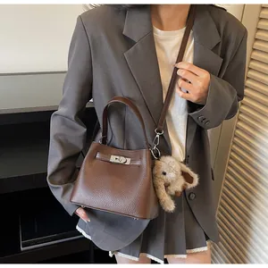 Detail of dark brown lychee grain leather bucket bag with silver lock and plush bunny