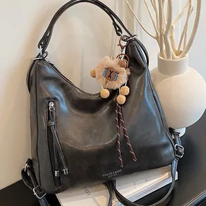 Vintage dark gray leather tote bag with fringe detail and plush bear charm on books