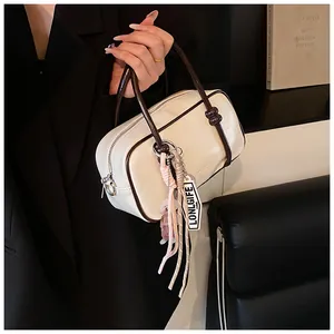 Détail du sac Boston crème avec bords contrastés, pompons et poignées nouées élégantes