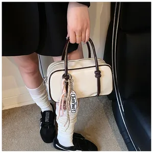 Détail du sac Boston crème avec anses marron porté par un mannequin en extérieur