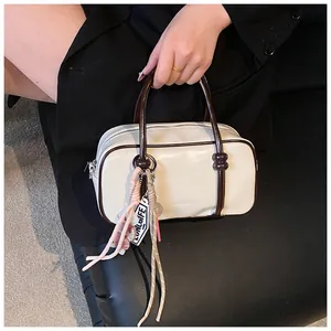 Détail du sac Boston en similicuir crème avec poignées brunes et pendentifs tressés