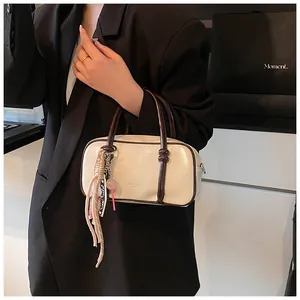 Détail du sac Boston en cuir verni blanc avec poignées marron et breloque pompon rose